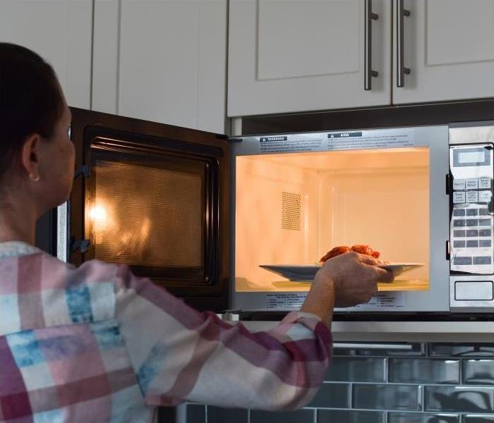 Woman placing a plate of food into a microwave