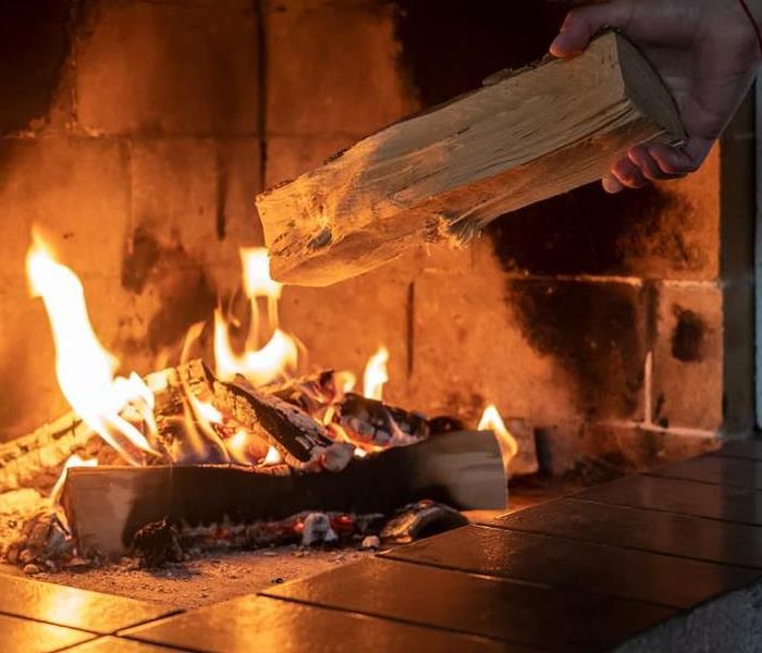 A man places a log into a fireplace fire.